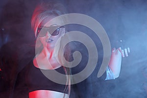 Woman rocker in sunglasses stands and smoke.