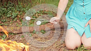 woman roes marshmallows on a fire. Sweet appetizing delicious treat on a stick. A fire in the fresh air, an active