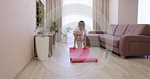 woman roll out pink yoga mat in living room at home