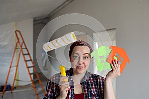 A woman with a roller in her hands is confused about choosing a painting color.