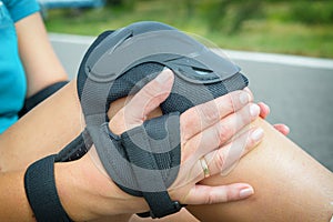 Woman rollerskater putting on knee protector pads on her leg