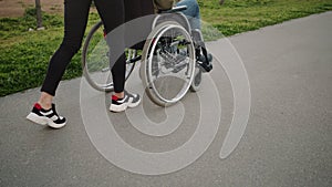 Woman is rolling invalid carriage with adult man outdoors, close-up of legs