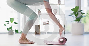 Woman rolling out a yoga mat on the floor in a yoga fitness training room. Active and fit barefoot female preparing for