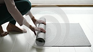 Woman rolling up exercise mat and preparing doing yoga or fitness.