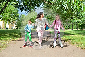 Woman rolls children`s hands on roller skates in a Sunny Park in