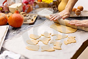 A woman rolls out dough for Halloween cookies with a wooden rolling pin.
