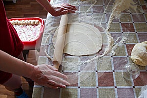 Woman rolls out dough with rolling pin in kitchen, close up