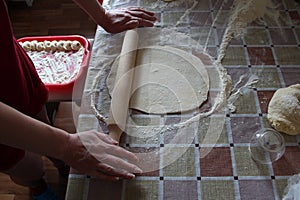 Woman rolls out dough with rolling pin in kitchen, close up