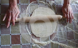 Woman rolls out dough with rolling pin in kitchen, top view, close up