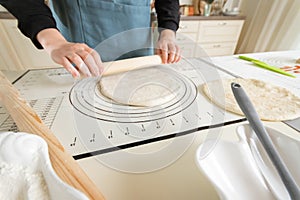A woman rolls out dough on a silicone baking mat with markings