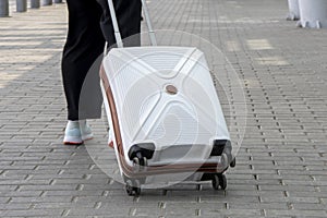 A woman rolls a white suitcase on wheels, close-up. Concept: hand Luggage on trips and trips, things on the road, going on vacatio