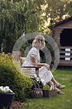 woman in romantic white dress relaxing in summer evening garden with glass of wine.