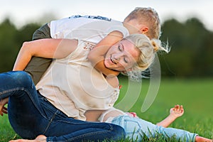 Woman romps with her two sons on the grass