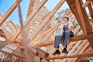 Woman roofer sitting on roof beam and enjoying done roofing works