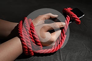 Woman with roped hands holding smart phone on grey background. Solitude concept