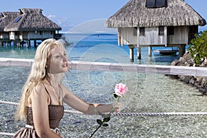 The woman with a rose in a hand looks at the sea and houses over water. Tahit