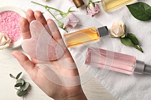 Woman with rose quartz gua sha tool at white wooden table, top view