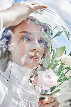 Woman with a round aquarium on her head holds flowers near her face. Concept of a girl cosmonaut and nature. Protection of nature
