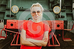 Woman in round stylish glasses stands in front of a train. Self-confidence, assertiveness