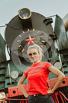 Woman in round stylish glasses stands in front of a train. Self-confidence, assertiveness