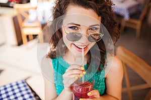 Woman in round sunglasses with cocktail at cafe terrace having fun