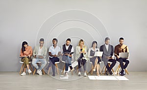 Woman in row with people who came for interview and are busy reading resumes or surfing internet.