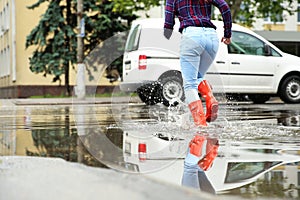 Woman with rubber boots running in puddle. Rainy weather