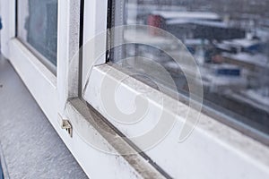 A woman in a rubber glove points to the mold. Plastic window and window sill in mold and dirt. Fungus and dampness at the wet