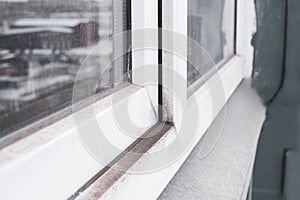 A woman in a rubber glove points to the mold. Plastic window and window sill in mold and dirt. Fungus and dampness at the wet