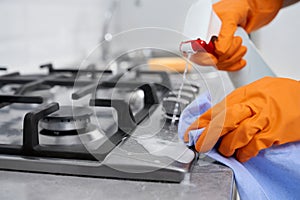 Woman in rubber gloves cleaning cooker with detergent.