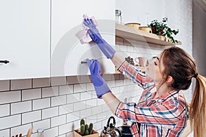 Woman in rubber gloves cleaning kitchen cabinet