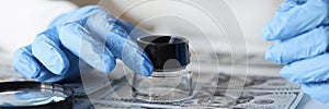 Woman in rubber gloves looking at dollar bills through magnifying glass