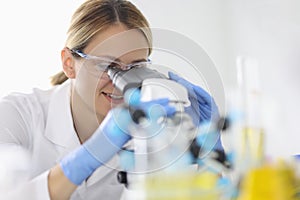Woman in rubber gloves and protective chemical glasses looks through microscope in laboratory portrait