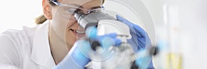 Woman in rubber gloves and protective chemical glasses looks through microscope in laboratory portrait