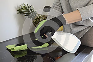 Woman with rubber protective gloves cleans the stove, induction plate  in the kitchen with the cleaning fluid.