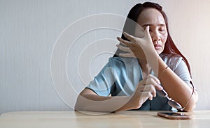 Woman rubbing her eyes feel painful with using smartphone sitting on the desk at home