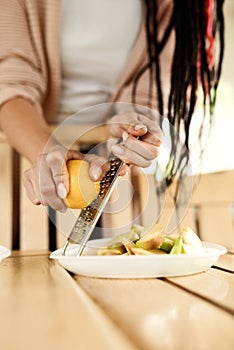 A woman rubs peel of lemon. Lemon peel and juice. Hand-held juice squeezer for citrus and graters on the kitchen table