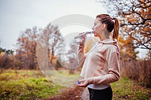 Woman runner drinks water in autumn forest