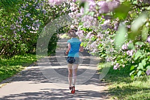 Woman runner jogging in spring park with lilac blossom, morning run outdoors, fitness and running