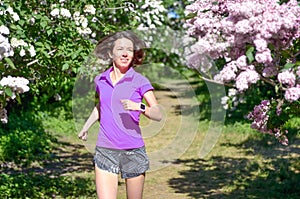 Woman runner jogging in spring park with lilac blossom, morning run outdoors, fitness and running