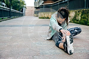Woman runner looking down while stretching leg before training on town