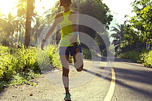 Woman runner stretching legs before running at morning tropical forest trail