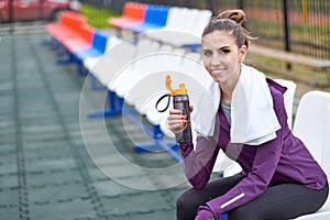 Woman runner with towel resting and drinking water from a bottle after working out track run of stadium