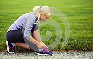 Woman runner tying running shoes. Blonde Girl over Grass