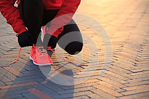 Woman runner tying shoelace in the sunrise sunshine