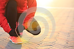 Woman runner tying shoelace in the sunrise sunshine