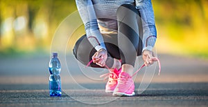 Woman runner tying shoelaces before jogging in autumn tree alley park. Sports female autumn outfit leggings and thermal underwear