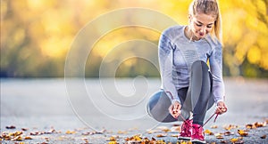 Woman runner tying shoelaces before jogging in autumn tree alley park. Sports female autumn outfit leggings and thermal underwear photo