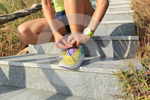 Woman runner tying shoelaces on stone trail