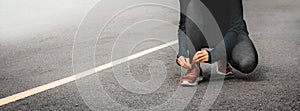 Woman runner tying shoes on road background